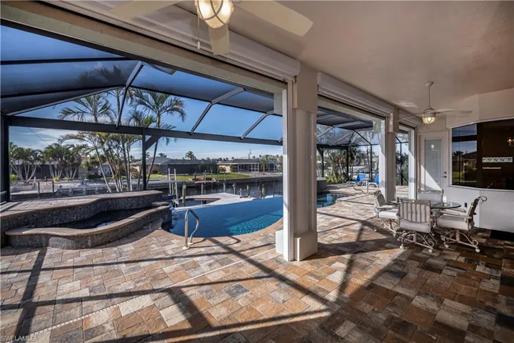 View of patio with ceiling fan, a pool with hot tub, and glass enclosure