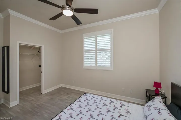 Bedroom with a walk in closet, ornamental  molding, ceiling fan, laminate flooring, and a closet