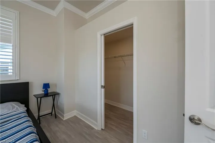 Bedroom with ornamental molding, a walk in closet, light hardwood / wood-style flooring, and a closet