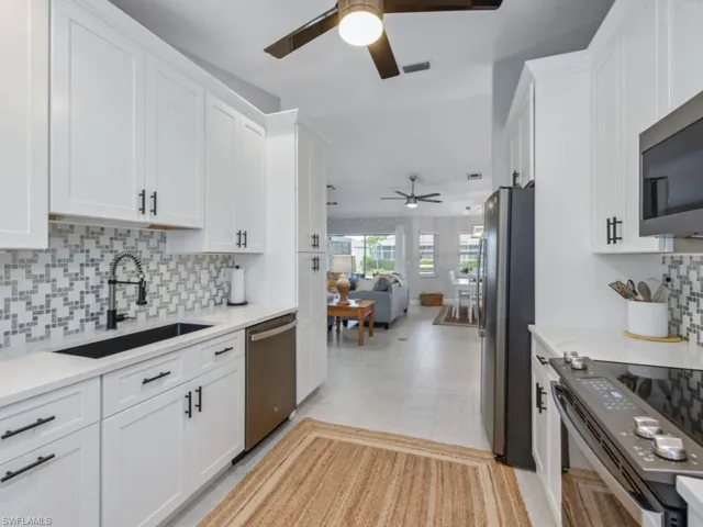 Kitchen featuring a ceiling fan, appliances with stainless steel finishes, white cabinetry, and backsplash