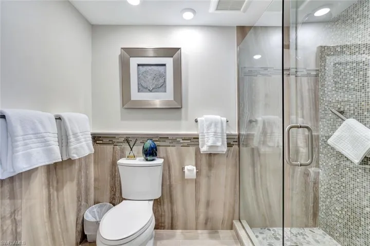 Full bath with tile walls, toilet, visible vents, and a stall shower
