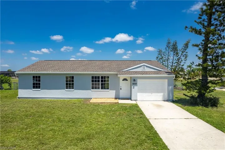 Ranch-style home featuring a garage, concrete driveway, a front lawn, and stucco siding