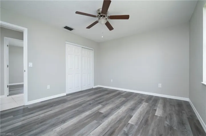 Unfurnished bedroom with dark wood-style floors, a closet, visible vents, and baseboards