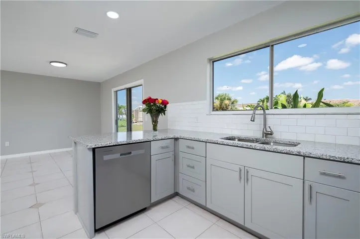 Kitchen with a sink, a peninsula, light stone counters, and stainless steel dishwasher