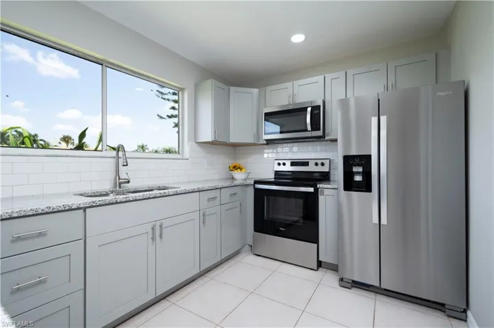 Kitchen with light tile patterned floors, light stone counters, stainless steel appliances, a sink, and decorative backsplash