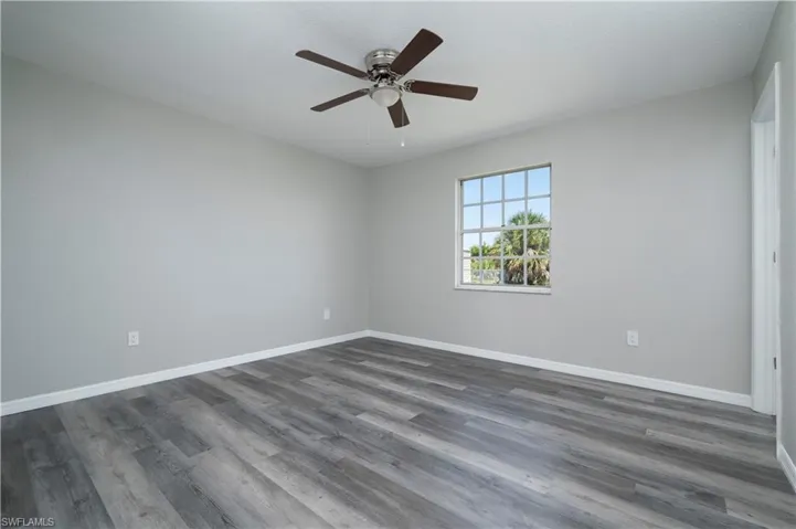 Unfurnished room featuring dark wood-type flooring, baseboards, and a ceiling fan