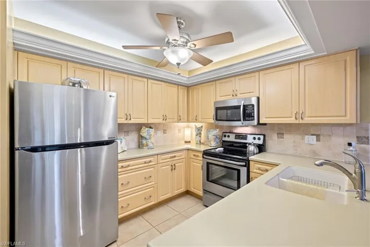 Kitchen featuring appliances with stainless steel finishes, tasteful tiled backsplash, double sink,solid surface counter tops, light tile patterned floors and ceiling fan