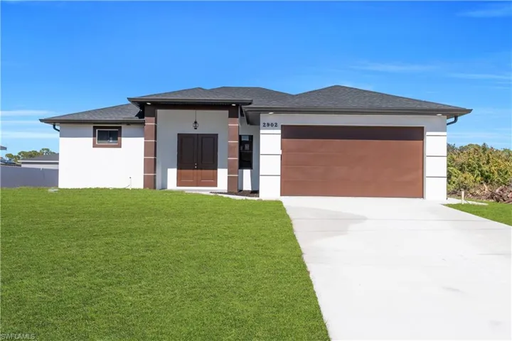 Prairie-style home with a front lawn, stucco siding, a shingled roof, and concrete driveway
