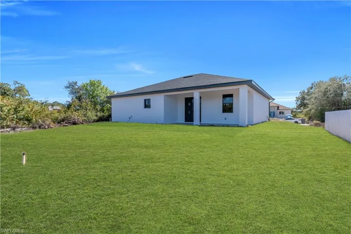Rear view of property featuring a lawn and stucco siding