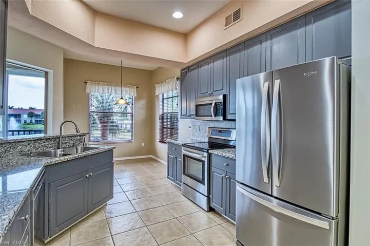 Kitchen featuring stainless steel appliances, light stone countertops, gray cabinets, light tile patterned flooring, and a raised ceiling