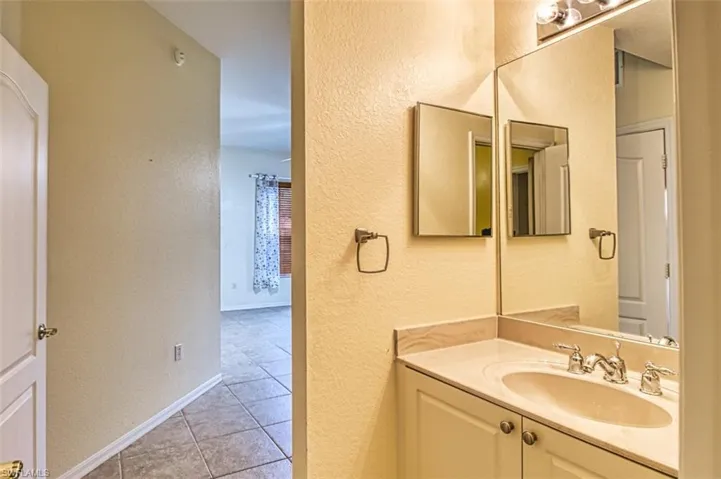 Bathroom with a textured wall, vanity, and light tile patterned flooring