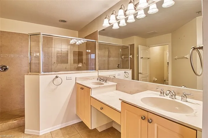 Bathroom featuring a walk in shower, double vanity, and light tile patterned flooring