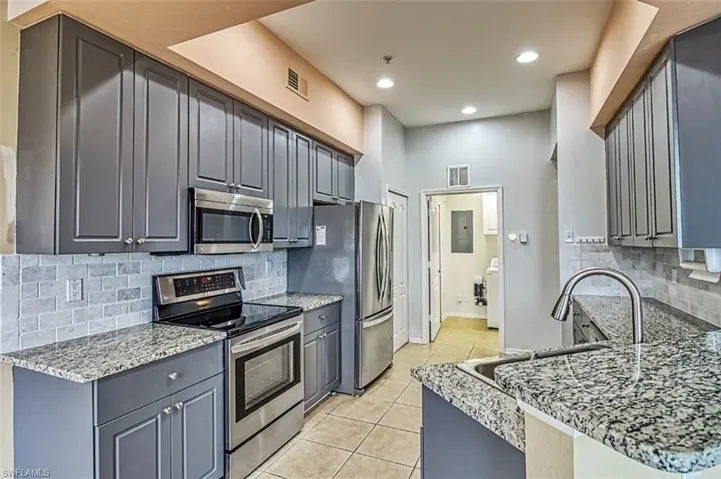 Kitchen with stainless steel appliances, gray cabinets, tasteful backsplash, light stone counters, and light tile patterned floors