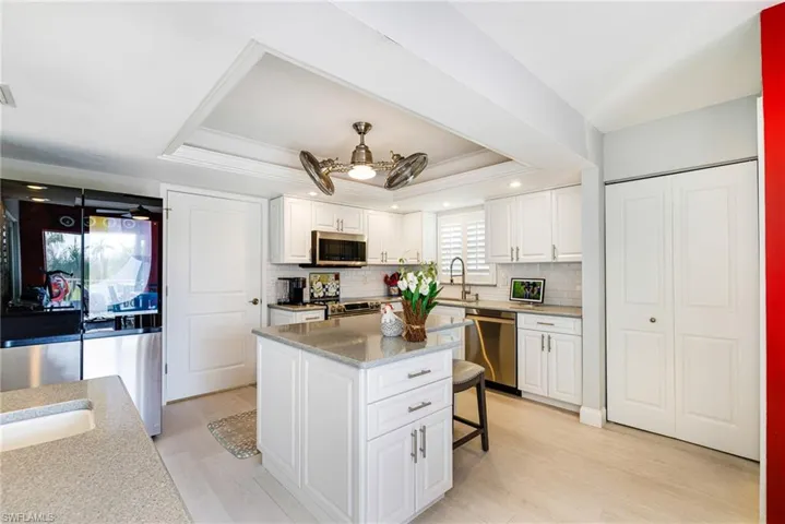 Kitchen with a tray ceiling, light wood-style flooring, appliances with stainless steel finishes, white cabinetry, and ornamental molding
