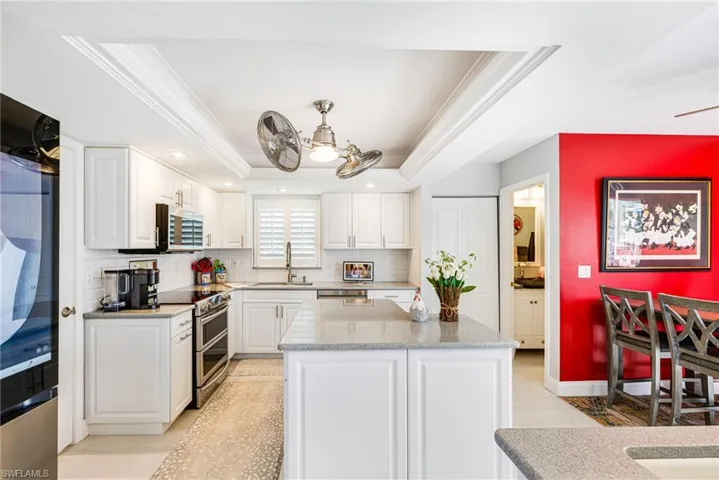 Kitchen featuring white cabinets, a tray ceiling, tasteful backsplash, appliances with stainless steel finishes, and ornamental molding