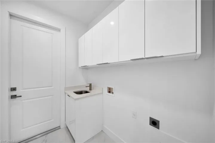 Laundry area with light tile patterned floors, hookup for a washing machine, cabinets, electric dryer hookup, and sink
