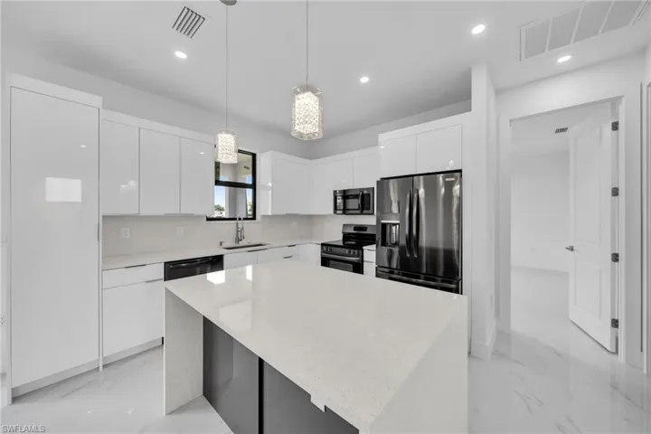 Kitchen featuring stainless steel appliances, white cabinets, sink, hanging light fixtures, and a kitchen island