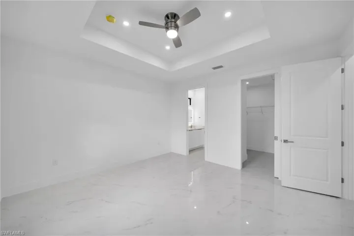 Unfurnished bedroom with a spacious closet, a tray ceiling, a closet, light tile patterned flooring, and ceiling fan