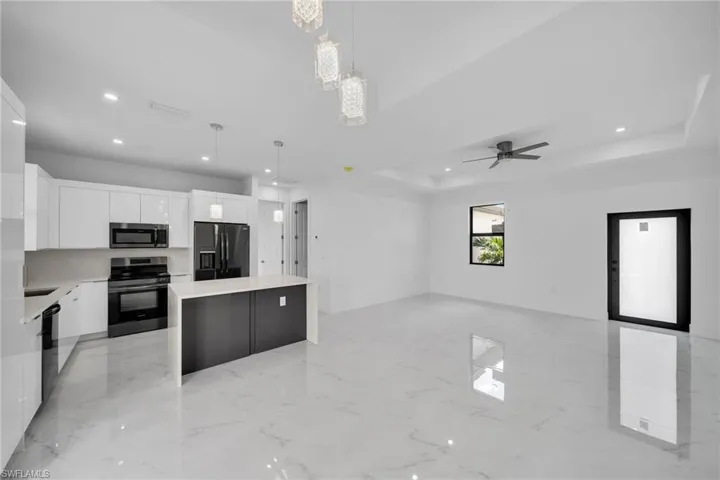 Kitchen with stainless steel appliances, pendant lighting, a kitchen island, white cabinetry, and a tray ceiling