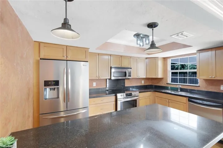 Kitchen featuring a raised ceiling, appliances with stainless steel finishes, decorative light fixtures, sink, and ornamental molding