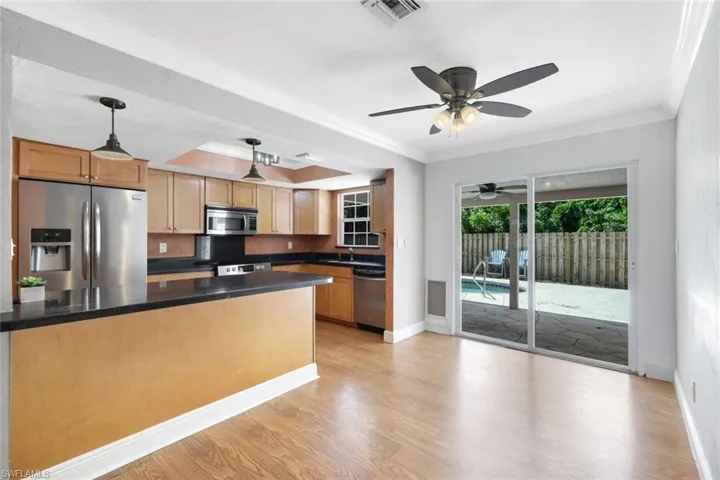 Kitchen with backsplash, ceiling fan, stainless steel appliances, light hardwood / wood-style floors, and decorative light fixtures