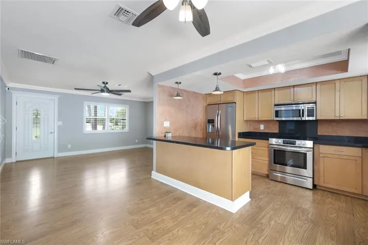 Kitchen featuring stainless steel appliances, decorative backsplash, light wood-type flooring, ceiling fan, and ornamental molding