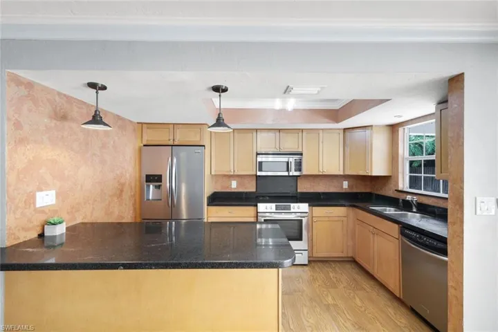 Kitchen with stainless steel appliances, light hardwood / wood-style flooring, hanging light fixtures, and light brown cabinetry