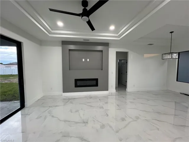 Unfurnished living room featuring a raised ceiling, a healthy amount of sunlight, and light tile flooring