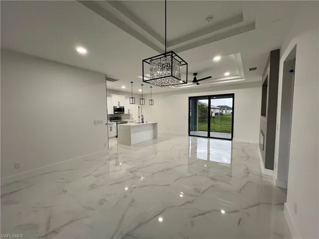 Unfurnished living room with light tile flooring, a raised ceiling, and ceiling fan with notable chandelier