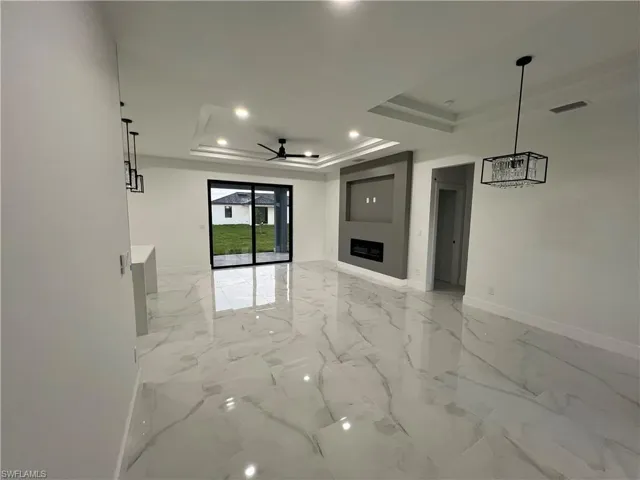 Unfurnished living room featuring ceiling fan, a tray ceiling, and light tile floors