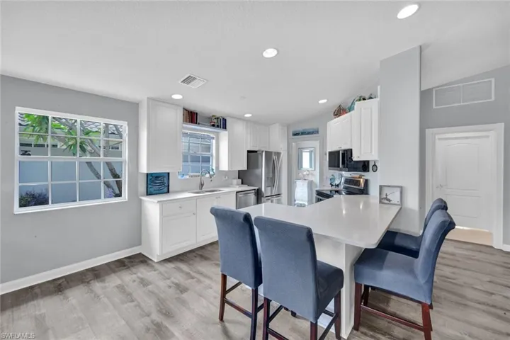 Contemporary kitchen featuring white cabinetry, light-toned countertops, stainless steel appliances, and wood-finish flooring