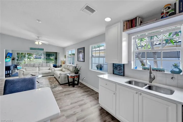 Open-concept living space featuring wood-finish flooring, vaulted ceilings, and a kitchen with white cabinetry, a double basin sink, and white countertops