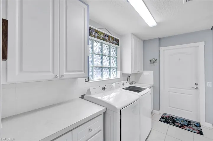 Dedicated utility space featuring ample white cabinetry, a glass block window, a durable countertop, and a built-in sink
