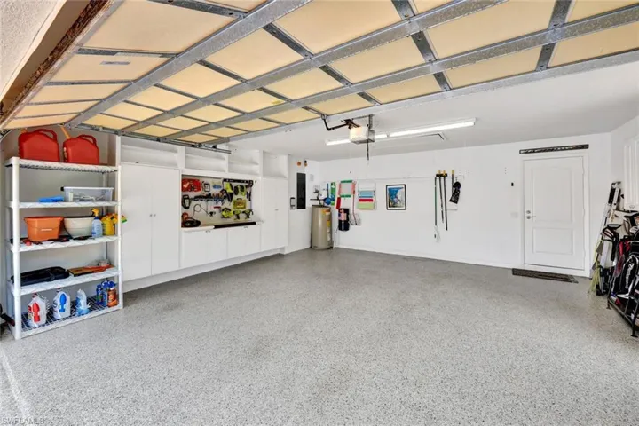 Spacious garage with an epoxy-coated concrete floor, extensive built-in white cabinetry, a dedicated workbench area, and bright overhead fluorescent lighting