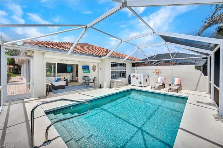 Screened-in pool area featuring a rectangular swimming pool with steps, a stainless steel handrail, and a surrounding concrete patio