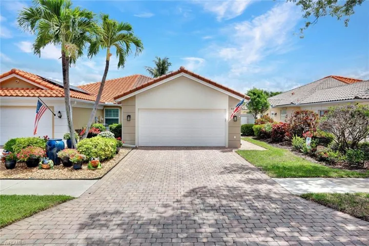 Exterior featuring a tile roof, stucco finish, paver driveway, mature landscaping, and an attached garage