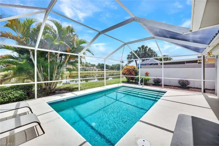 Screened-in outdoor living space featuring a rectangular pool with light blue tiling, a concrete pool deck, and landscaping with mature palm trees