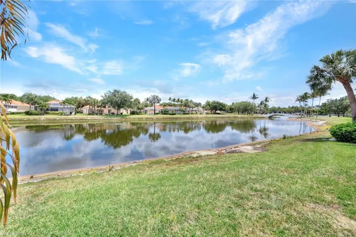 Expansive lakefront setting featuring a manicured lawn, mature palm trees, and a distant pedestrian bridge