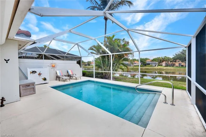 Screened enclosure featuring a rectangular pool with steps and handrail, concrete decking, and a water view