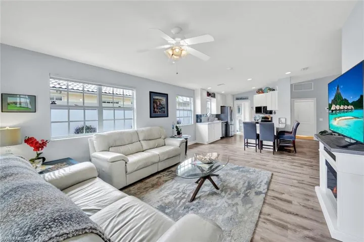 Open-concept living area featuring wood-finish flooring, a ceiling fan, and multiple windows