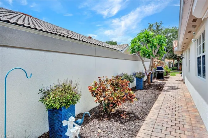 Paved brick walkway bordered by mature landscaping and a stucco privacy wall