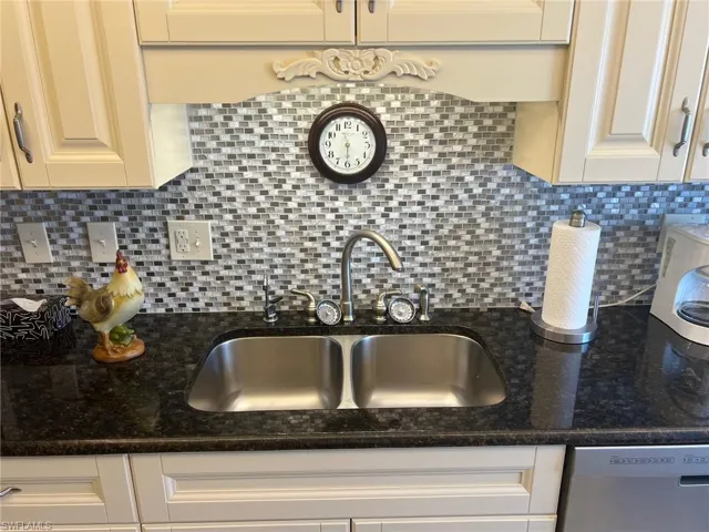 Kitchen with dishwasher, a sink, dark stone countertops, and tasteful backsplash