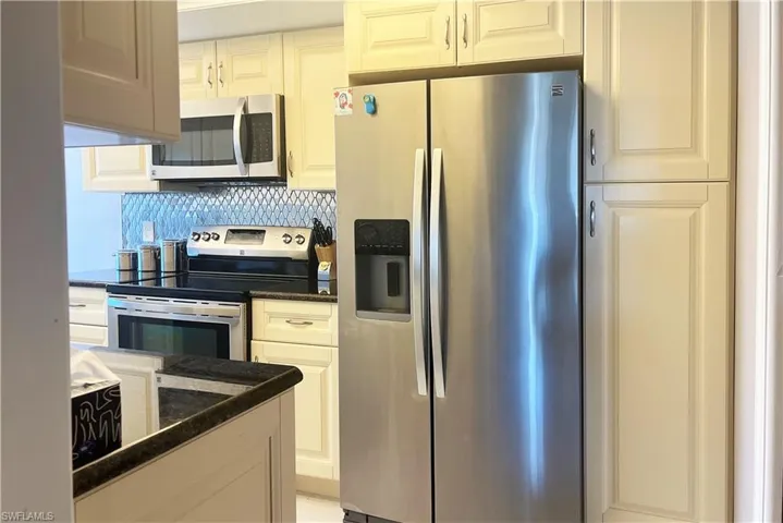 Kitchen featuring dark stone counters, appliances with stainless steel finishes, and tasteful backsplash