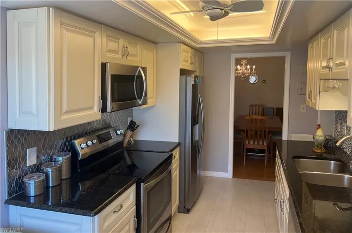 Kitchen featuring a sink, backsplash, ceiling fan with notable chandelier, appliances with stainless steel finishes, and a raised ceiling