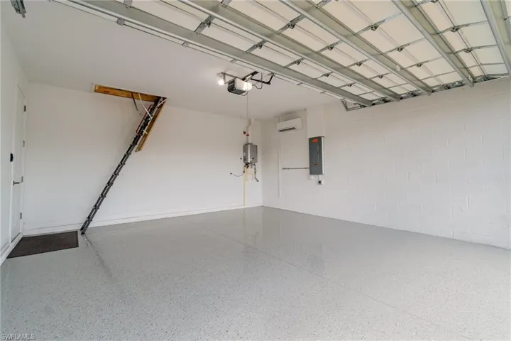 Garage featuring electric panel, a garage door opener, an AC wall unit, concrete block wall, and water heater