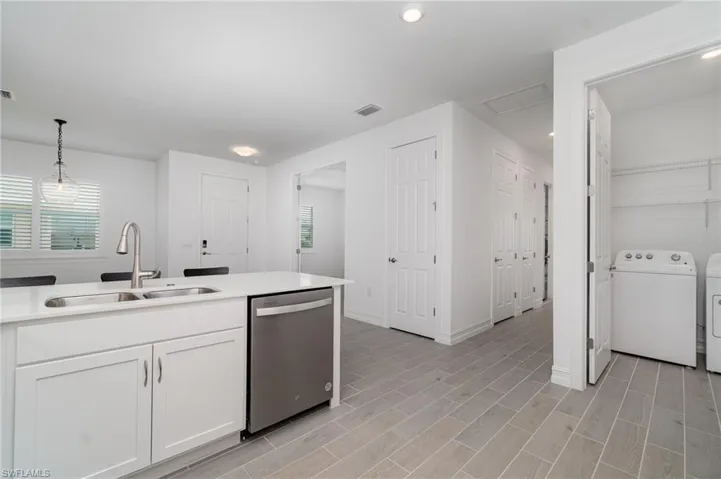 Kitchen featuring dishwasher, washing machine and clothes dryer, white cabinetry, hanging light fixtures, and light countertops