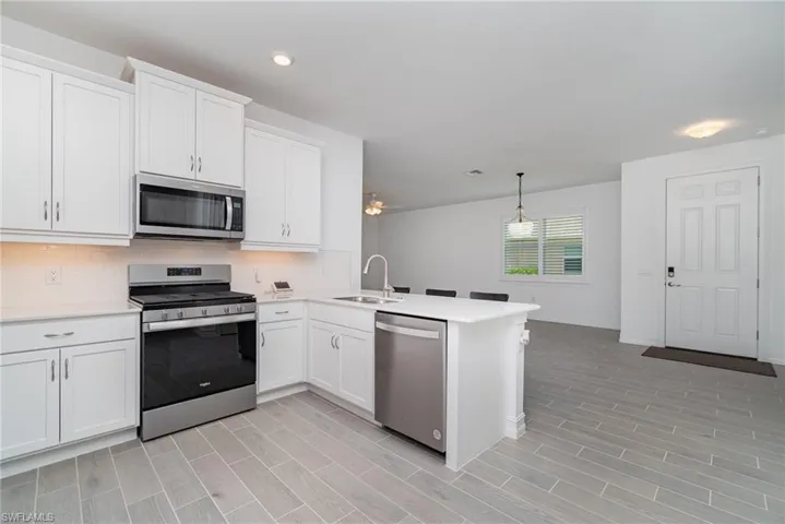 Kitchen featuring appliances with stainless steel finishes, light countertops, a peninsula, white cabinetry, and light wood-type flooring