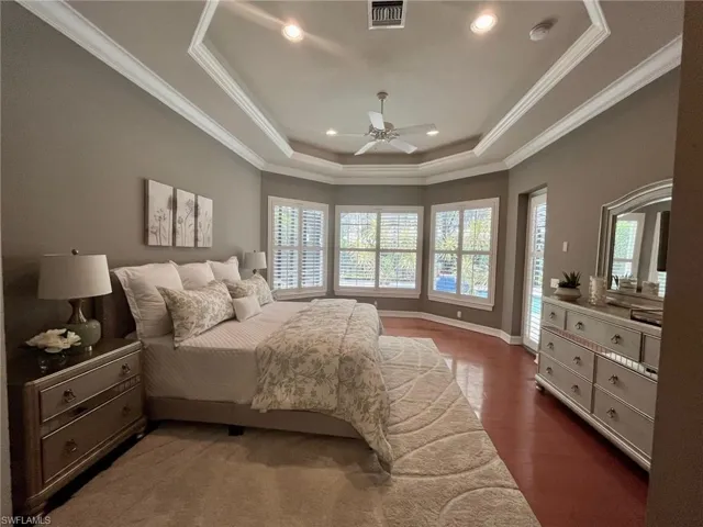 Bedroom with ceiling fan, a raised ceiling, crown molding, and dark wood-type flooring