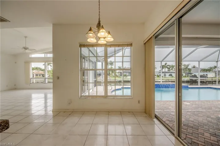 Doorway featuring light tile patterned flooring, lofted ceiling, and ceiling fan with notable chandelier