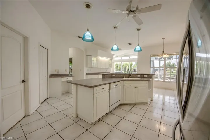 Kitchen with hanging light fixtures, dishwasher, a kitchen island, stainless steel refrigerator, and light tile patterned floors, Built in Desk, Large Pantry and entrance to Laundry Room to the left